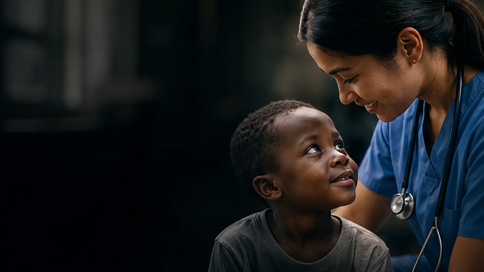 A clinician in scrubs smiles down at a young patient.